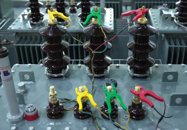 Color-coded test leads clamped to transformer bushings for voltage ratio and phase displacement test